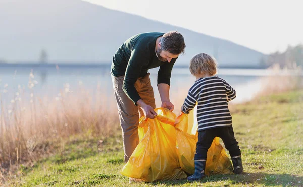 Father with small son collecting rubbish outdoors in nature, plogging concept. — Stock Photo, Image