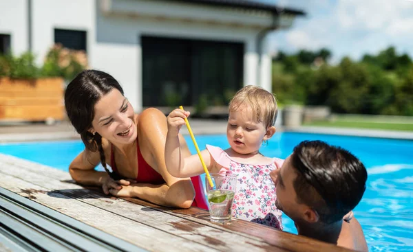 在后院花园的室外游泳池里带着小女儿的年轻家庭. — 图库照片