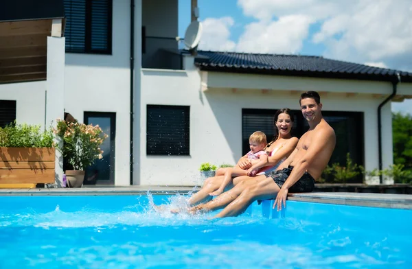 Молодая семья с маленькой дочкой в бассейне на открытом воздухе в саду. — стоковое фото