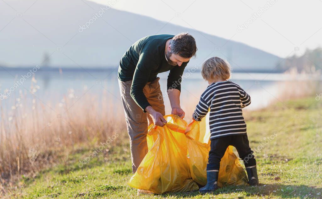 Father with small son collecting rubbish outdoors in nature, plogging concept.