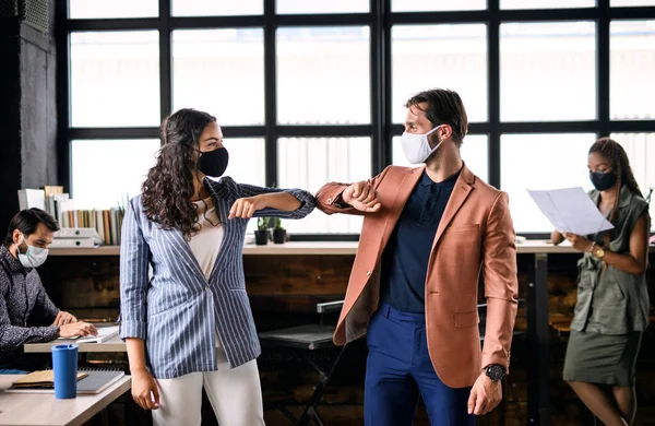 Young businesspeople with face masks working indoors in office, greeting. — Stock Photo, Image