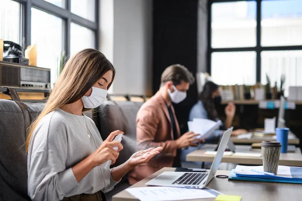 Porträtt av unga företagare med ansiktsmasker som arbetar inomhus på kontoret, desinficera händer. — Stockfoto