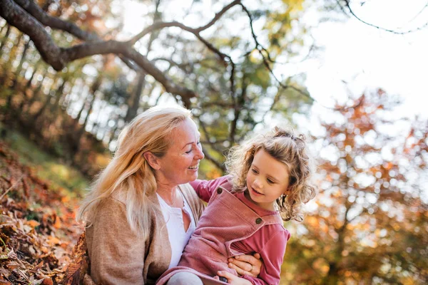 Small girl with grandmother on a walk in autumn forest, having fun. — Stock Photo, Image