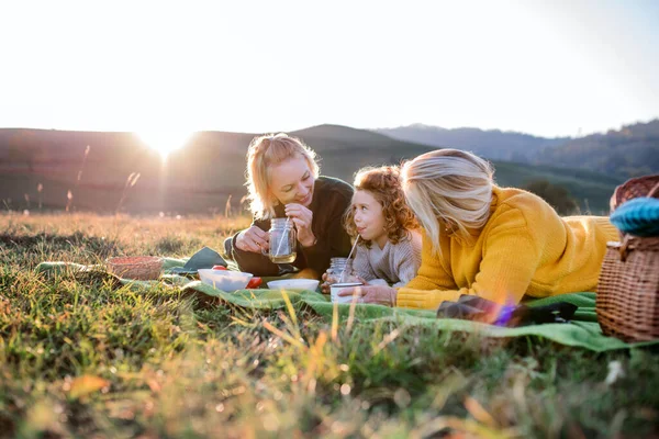 Kleines Mädchen mit Mutter und Großmutter beim Picknick in der Natur bei Sonnenuntergang. — Stockfoto