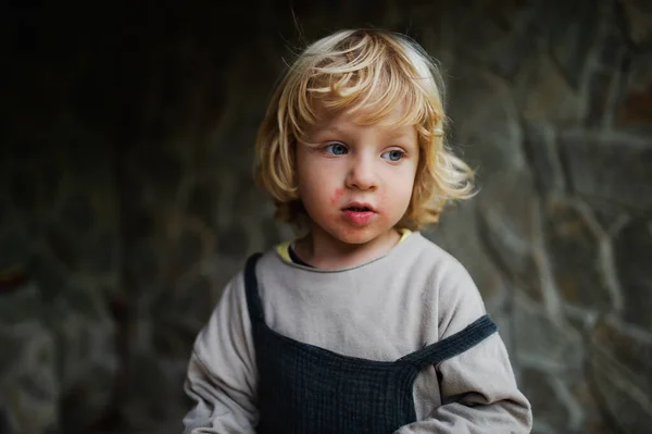 Close-up portrait of small boy standing outdoors, stone wall in the background. — Stock Photo, Image