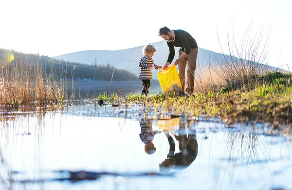 Vader met kleine zoon verzamelen van afval buiten in de natuur, plogging concept. — Stockfoto