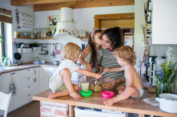 Zwangere vrouw met drie kleine kinderen binnen thuis, het bereiden van het ontbijt. — Stockfoto