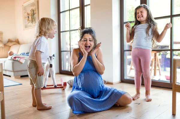 Mulher grávida infeliz com crianças pequenas gritando dentro de casa. — Fotografia de Stock