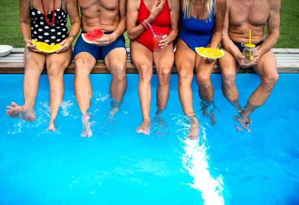 Група невпізнаваних літніх людей, які сидять біля басейну на відкритому повітрі на задньому дворі . — стокове фото