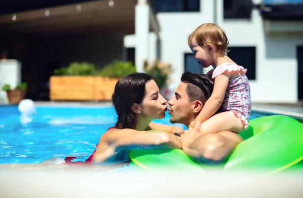 Familia joven con hija pequeña en piscina al aire libre en el jardín del patio trasero, besándose. —  Fotos de Stock