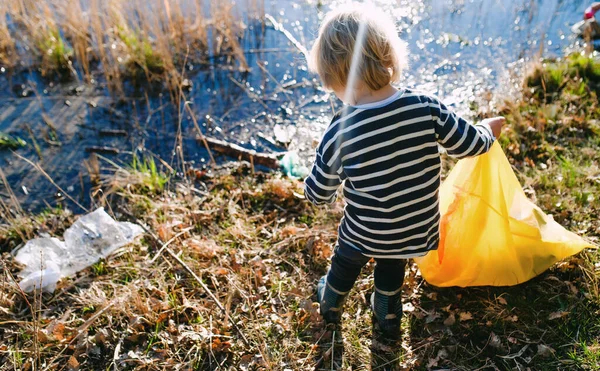 Piccolo bambino irriconoscibile che raccoglie spazzatura all'aperto in natura, concetto di plogging. — Foto Stock