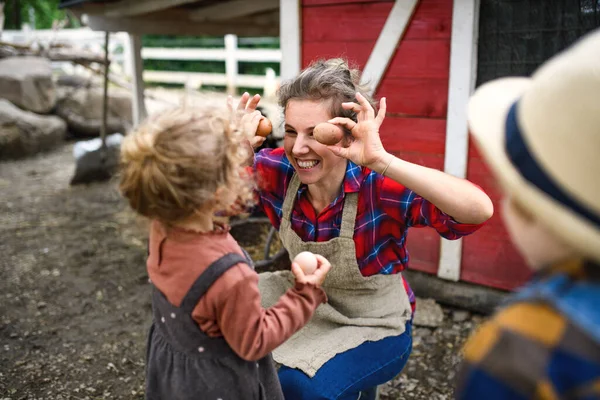 Ibu ceria dengan anak-anak kecil berdiri di pertanian, mengumpulkan telur. — Stok Foto
