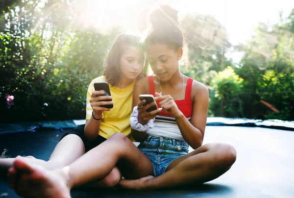 Pandangan depan gadis-gadis remaja teman-teman luar ruangan di kebun, menggunakan smartphone. — Stok Foto