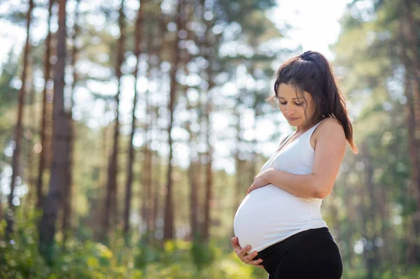 Portrét šťastné těhotné ženy venku v přírodě, dotýkající se jejího břicha. — Stock fotografie