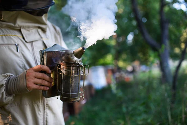A méhészetben dolgozó, felismerhetetlen méhész méhfüstölőt használ. — Stock Fotó