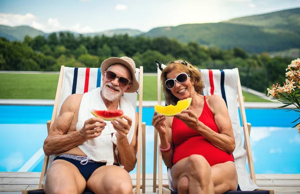 Cheerful senior couple sitting by swimming pool outdoors in backyard. — Stock Photo, Image