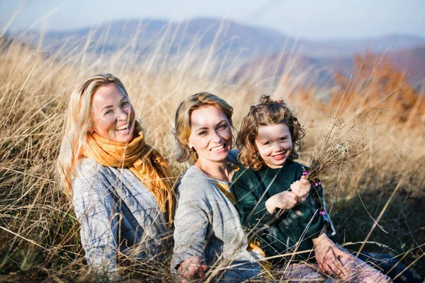 Klein meisje met moeder en grootmoeder rustend in de herfst natuur. — Stockfoto