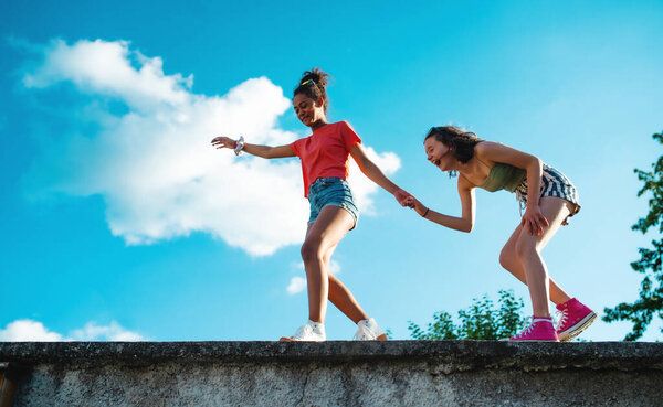 Young teenager girls friends outdoors in city, standing on concrete wall.