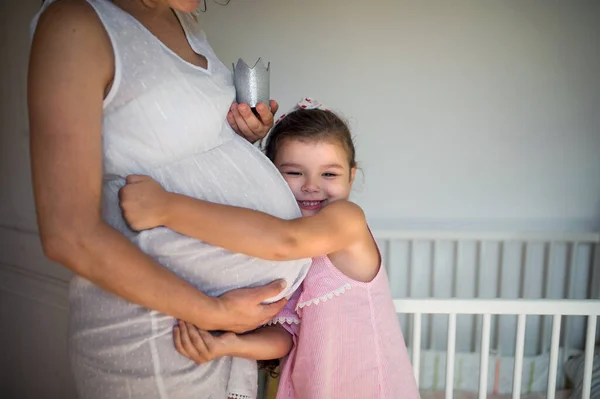 Retrato de una mujer embarazada con una hija pequeña en el interior de casa, abrazándose. — Foto de Stock