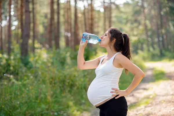 야외에서 수영을 한 후에 물을 마시는 임신 한 여자. — 스톡 사진