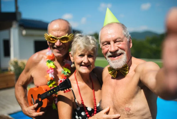 Groep van vrolijke senioren door het zwembad buiten in de achtertuin, het nemen van selfie. — Stockfoto