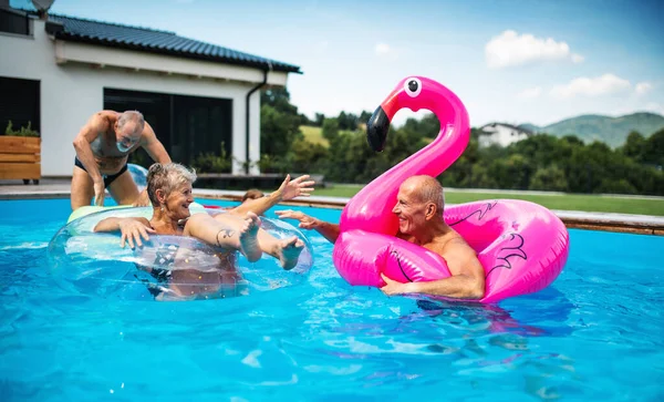 Grupo de personas mayores alegres en la piscina al aire libre en el patio trasero, hablando. — Foto de Stock