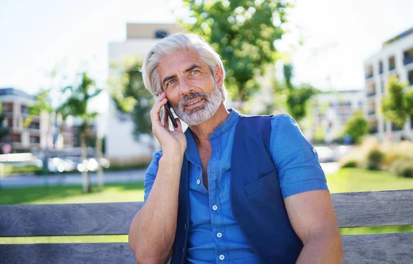 Portrait d'homme mature assis à l'extérieur en ville, à l'aide d'un smartphone. — Photo