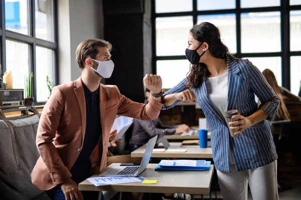 Business people with face masks greeting indoors in office, coronavirus concept. — Stock Photo, Image