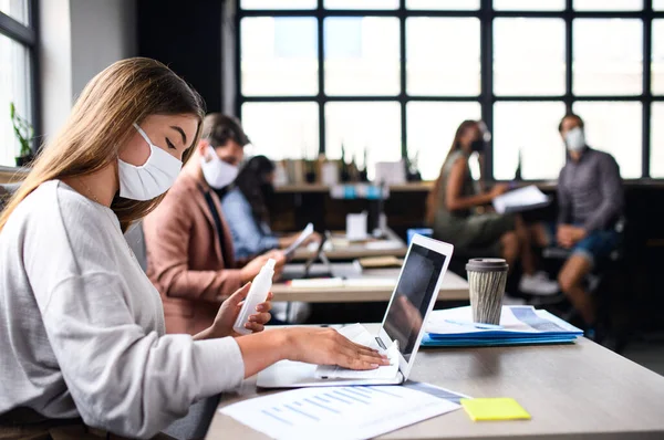 Pessoas com máscaras faciais desinfectando dentro de casa no escritório, de volta ao trabalho após o bloqueio do coronavírus. — Fotografia de Stock