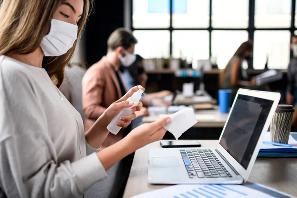 People with face masks disinfecting indoors in office, back to work after coronavirus lockdown. — Stock Photo, Image