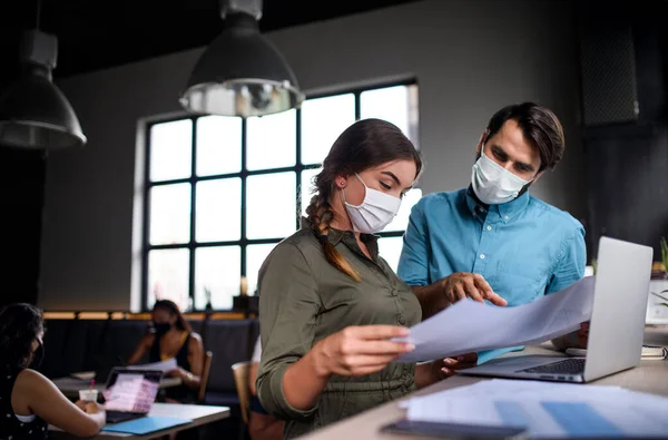 Business people with face masks indoors in office, back to work after coronavirus lockdown.