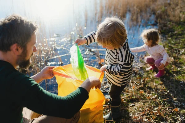 Otec s malými dětmi sbírající odpadky venku v přírodě, koncept plogování. — Stock fotografie