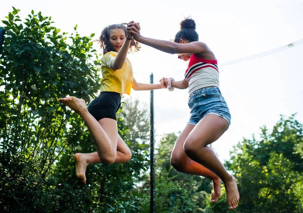 Low angle view of young teenager girls friends outdoors in garden, jumping on trampoline. — Stock Photo, Image