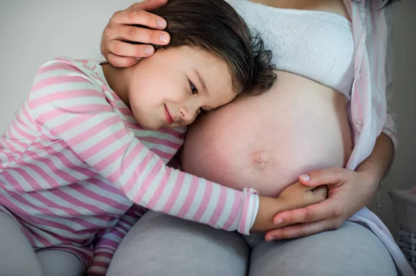 Портрет беременной женщины с маленькой дочерью в помещении дома, обнимающей. — стоковое фото