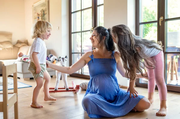 Mulher grávida com crianças pequenas dentro de casa, brincando. — Fotografia de Stock