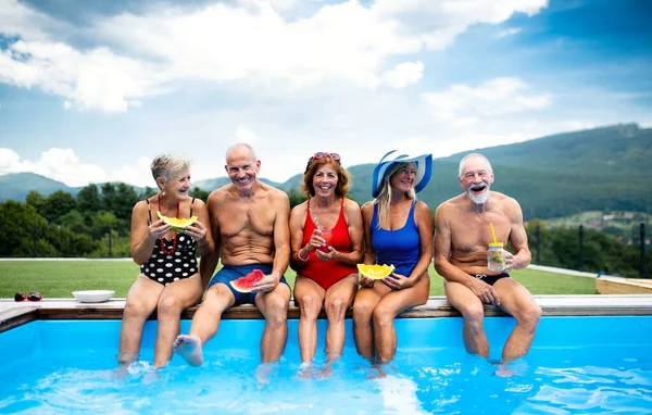 Vidám idősek csoportja, akik a szabadtéri medence mellett ülnek a kertben.. — Stock Fotó