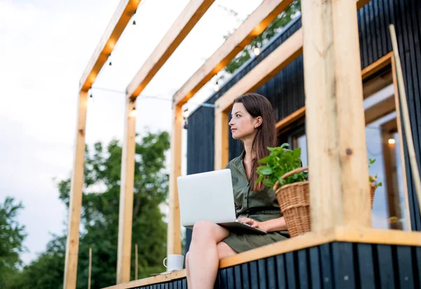 Ung kvinna med laptop utomhus, helg i container hus på landet. — Stockfoto