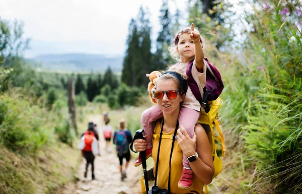 小さな幼児の娘が屋外で夏の自然をハイキングしている母親、カメラを見て. — ストック写真
