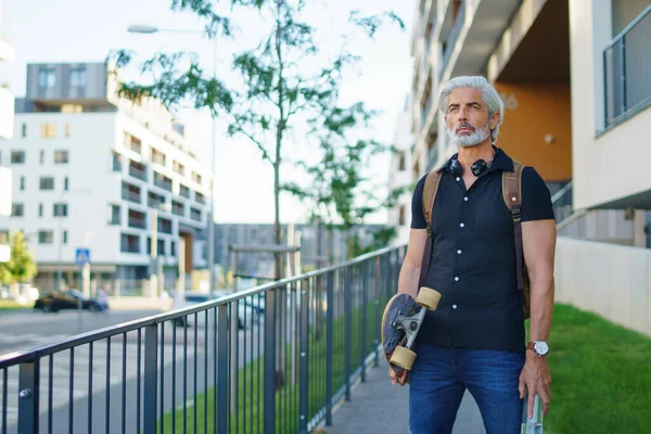スケートボードを持つ成熟した男の肖像は、都市の屋外で、仕事に戻る. — ストック写真