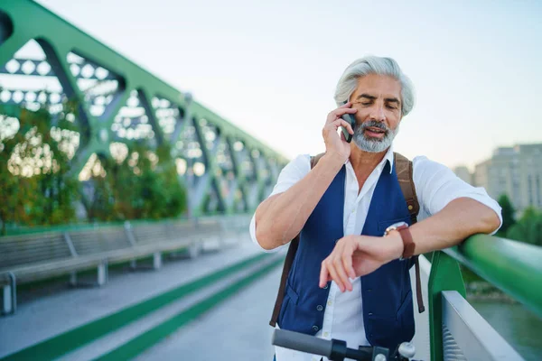 Portrait d'homme mature avec scooter électrique à l'extérieur en ville, à l'aide d'un smartphone. — Photo