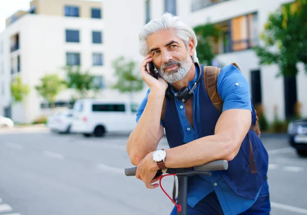 Şehirde elektrikli scooter kullanan, akıllı telefon kullanan, olgun bir adam..