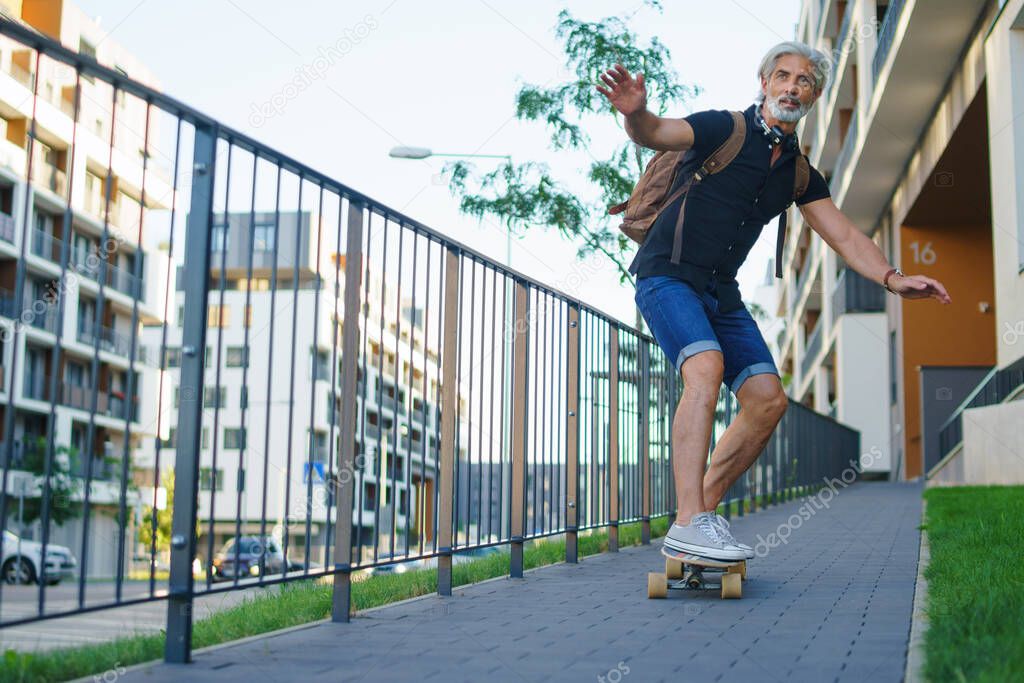 Portrait of mature man riding skateboard outdoors in city, going back to work.