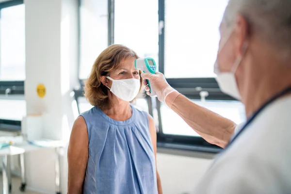 Läkare med ansiktsmask som mäter temperatur, coronavirus, covid-19, mättemperatur och vaccinationskoncept. — Stockfoto