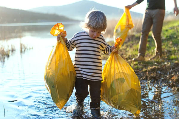 Padre con piccolo figlio che raccoglie spazzatura all'aperto in natura, concetto di plogging. — Foto Stock