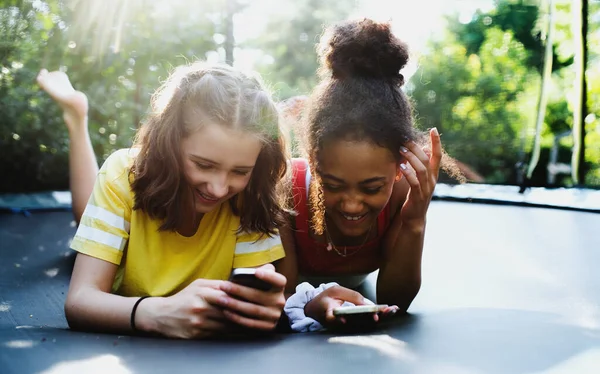 Vista frontal de jovens amigas adolescentes ao ar livre no jardim, usando smartphone. — Fotografia de Stock