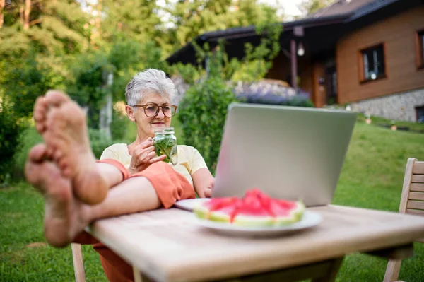 Щаслива старша жінка з ноутбуком, що працює на відкритому повітрі в саду, концепція домашнього офісу . — стокове фото