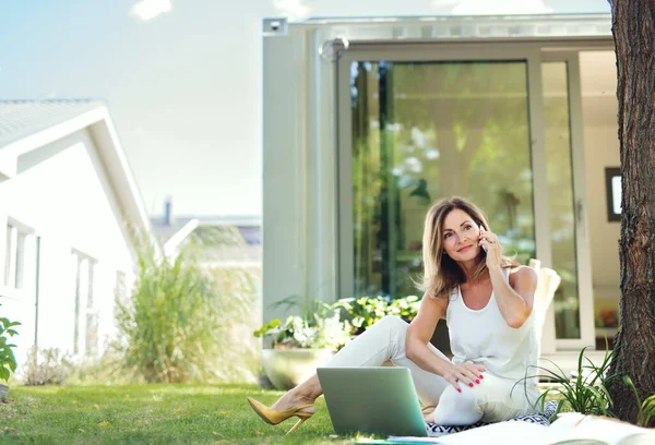 Mujer madura que trabaja en casa oficina al aire libre en el jardín, utilizando el teléfono inteligente. —  Fotos de Stock