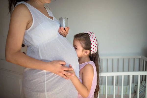 Small girl kissing belly of unrecognizable pregnant mother indoors at home. — Stock Photo, Image