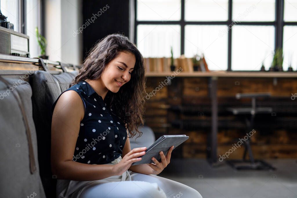 Portrait of young businesswoman indoors in office, using tablet.