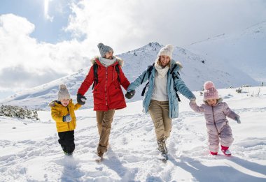 Anne ve baba kışın iki küçük çocukla karda yürüyorlar..